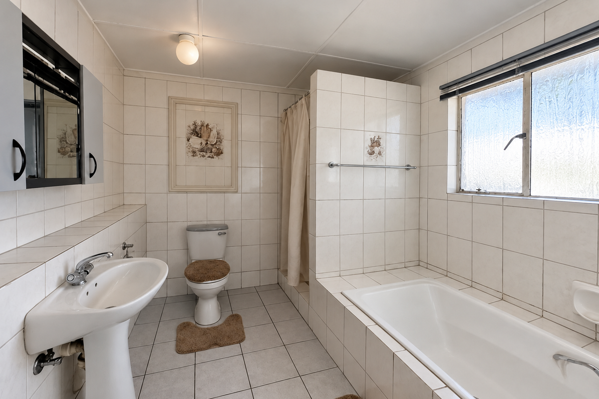 A functional bathroom featuring a pedestal basin, toilet, and a built-in bathtub with a shower area, finished with neutral wall and floor tiles.