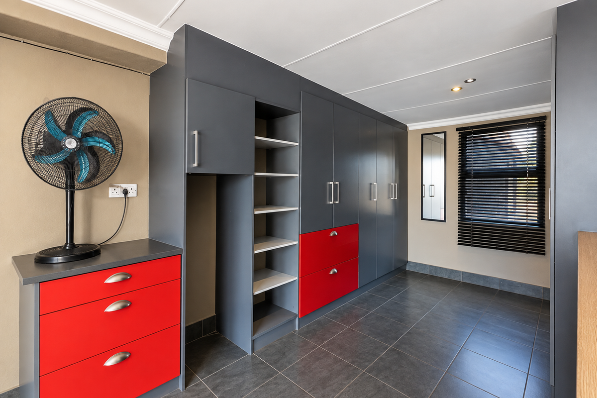 A modern bedroom featuring extensive built-in cabinetry with a bold red and grey finish, tiled flooring, and venetian blinds.