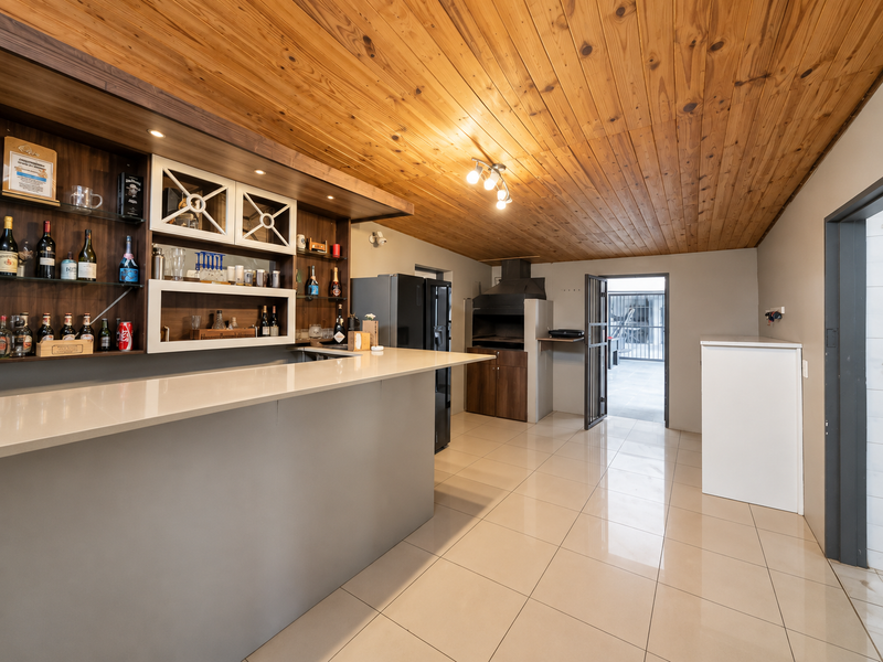 A well-appointed indoor bar area featuring a built-in counter, timber ceiling, and integrated braai, providing a functional space for entertaining.