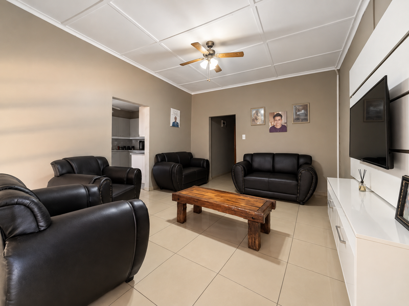 A spacious living room featuring neutral wall tones, large format floor tiles, a ceiling fan, and a built-in media unit.