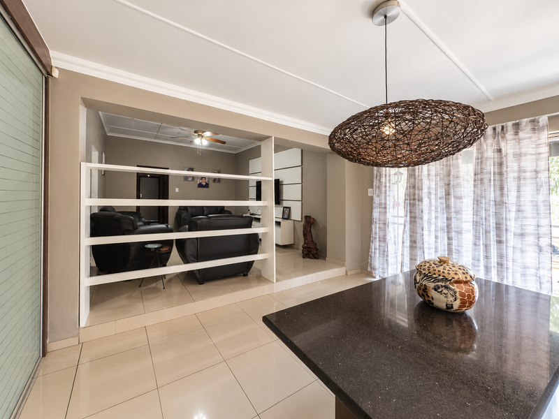 Spacious open-plan living area featuring tiled flooring, a built-in room divider, and a modern ceiling fan, creating a bright and functional living space.