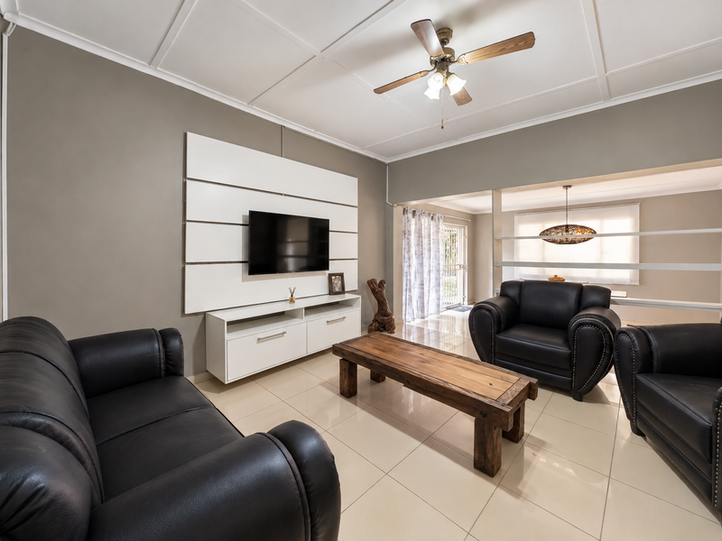 A well-maintained living room featuring tiled flooring, a coffered ceiling with a central fan, and a modern built-in media wall unit.