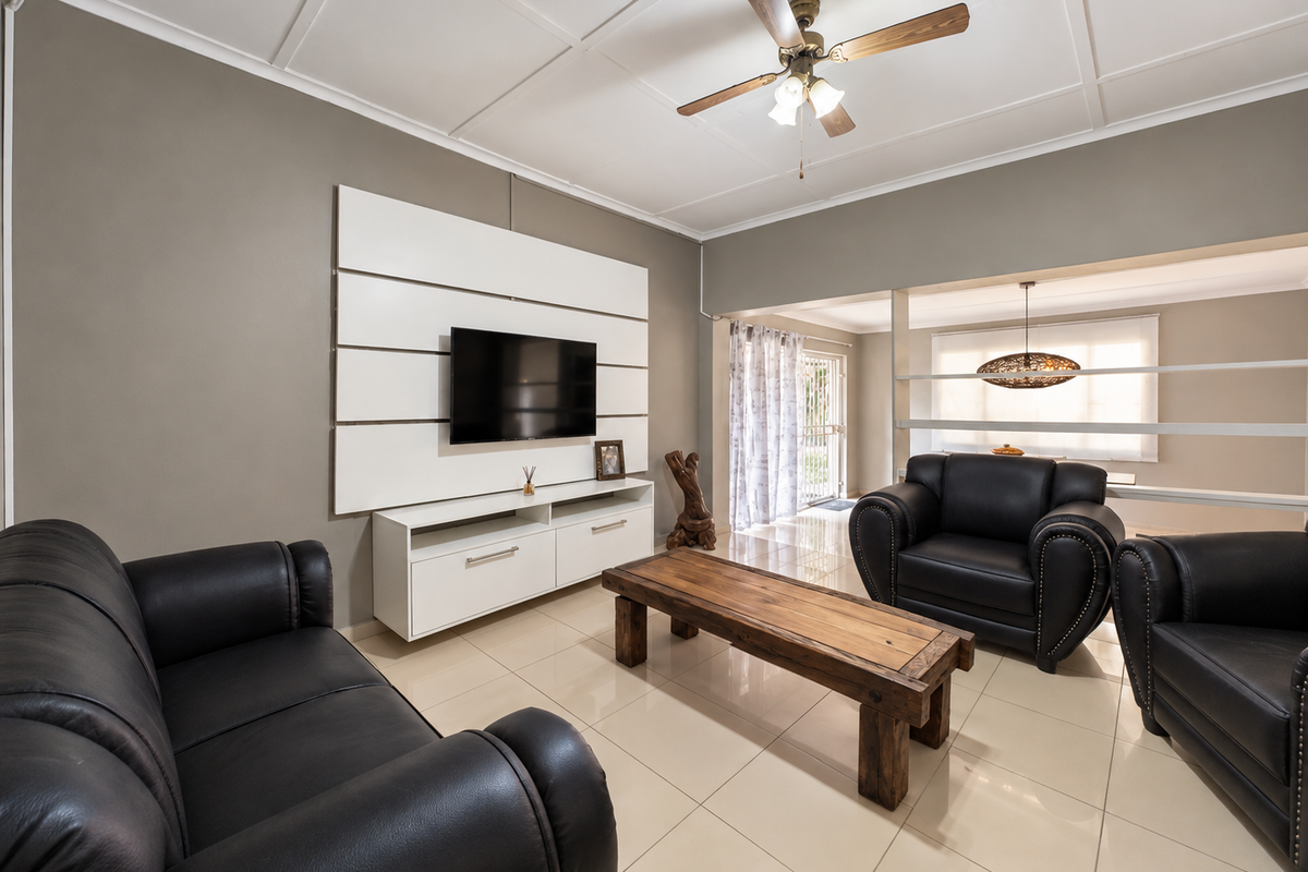A well-maintained living room featuring tiled flooring, a coffered ceiling with a central fan, and a modern built-in media wall unit.