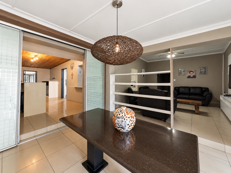 Open plan living and dining area featuring tiled flooring, sliding glass room dividers, and a central pendant light fixture connecting to the kitchen space.