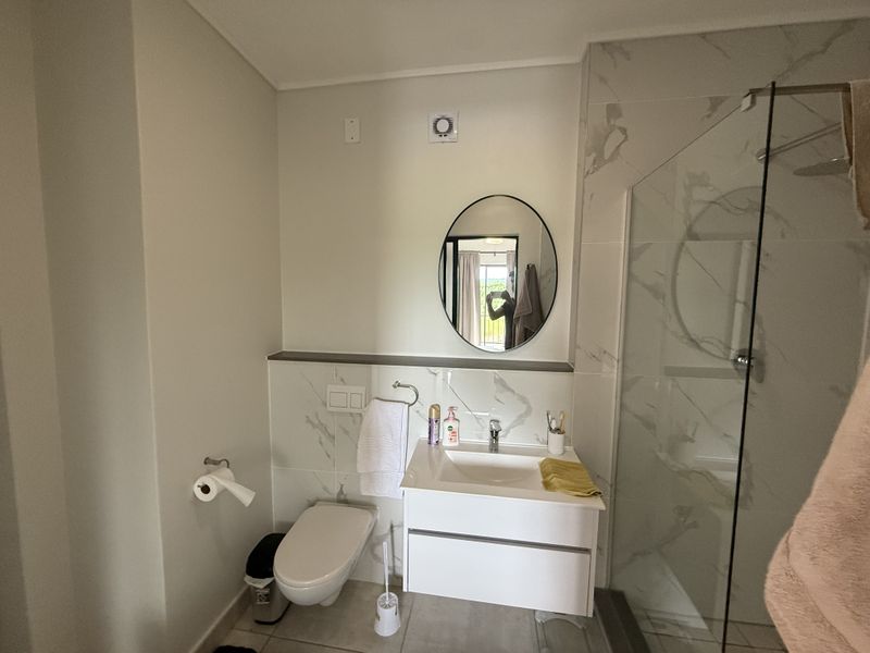 Modern bathroom featuring a wall-mounted toilet, vanity cabinet with integrated sink, and a glass-enclosed shower with marble-look wall tiles.