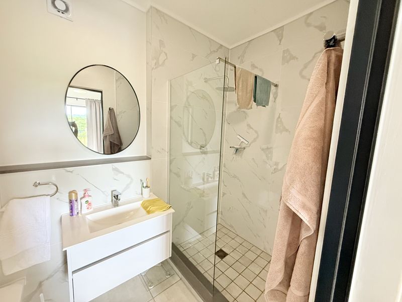 Modern bathroom featuring a sleek vanity, marble-look wall tiling, and a spacious walk-in shower with a glass screen.
