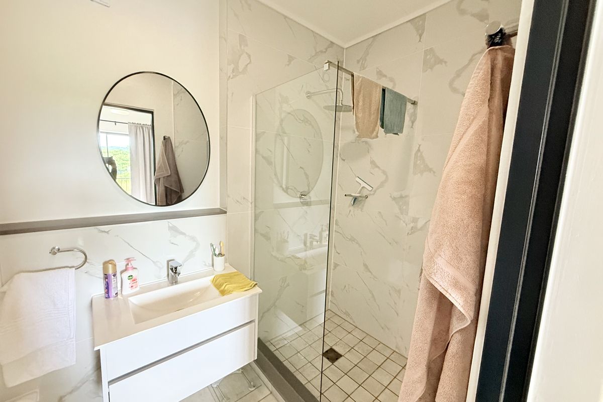 Modern bathroom featuring a sleek vanity, marble-look wall tiling, and a spacious walk-in shower with a glass screen.