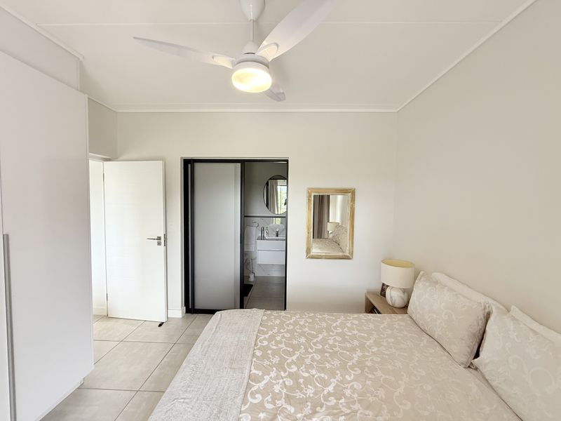 A well-maintained bedroom featuring tiled flooring, a ceiling fan, built-in wardrobe, and direct access to an en-suite bathroom.