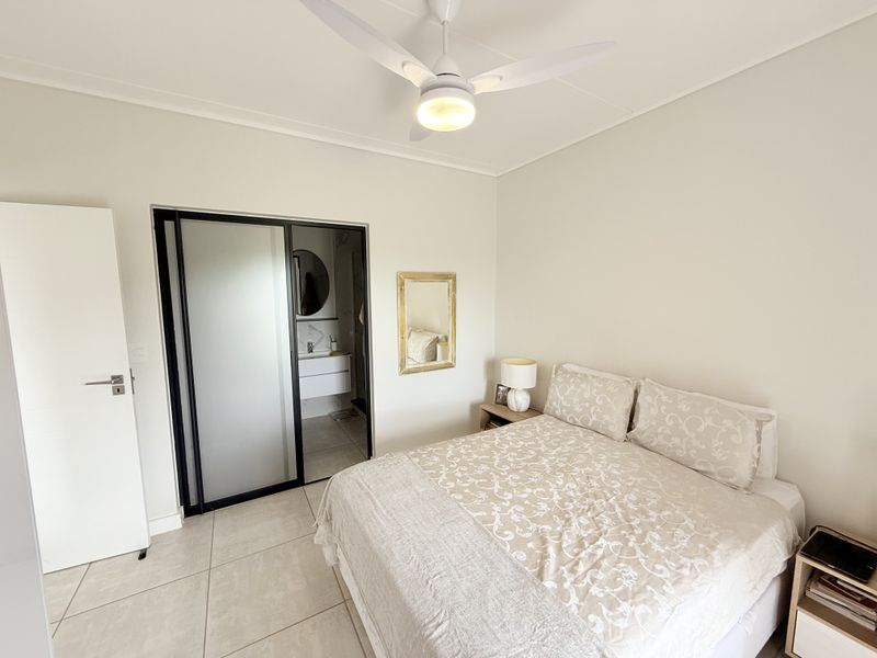 A well-maintained bedroom featuring neutral tiled flooring, a modern ceiling fan, and direct access to an en-suite bathroom through a sliding door.