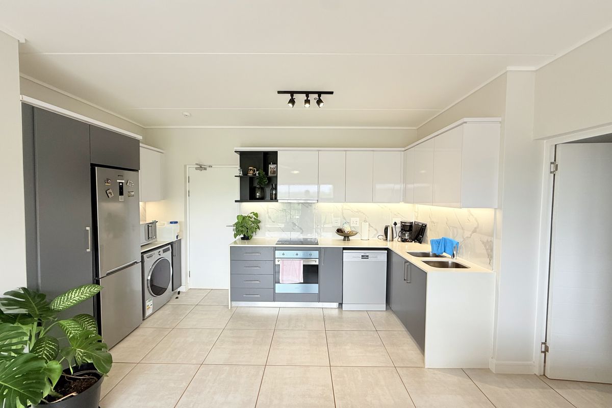 Modern kitchen featuring sleek two-tone cabinetry, stone countertops, marble-effect splashback, integrated appliances, and high-quality tiled flooring in a bright, open-plan layout.