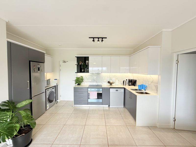 Modern kitchen featuring sleek two-tone cabinetry, stone countertops, marble-effect splashback, integrated appliances, and high-quality tiled flooring in a bright, open-plan layout.