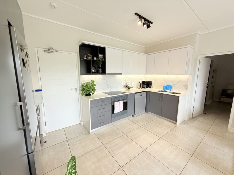 Modern kitchen featuring grey and white cabinetry, stone countertops, marble-look splashback, integrated dishwasher, and built-in oven with electric hob.