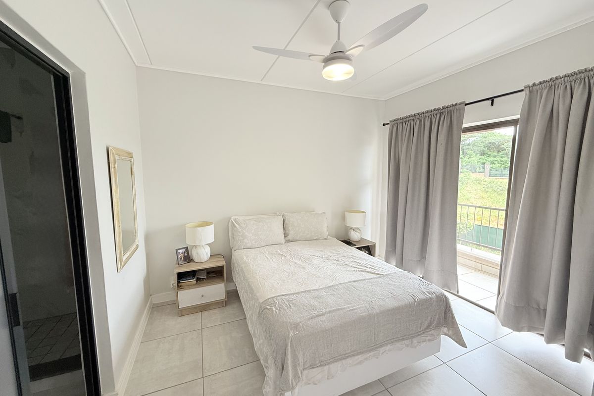 A bright bedroom featuring tiled flooring, a ceiling fan, and direct access to a private balcony through sliding glass doors.