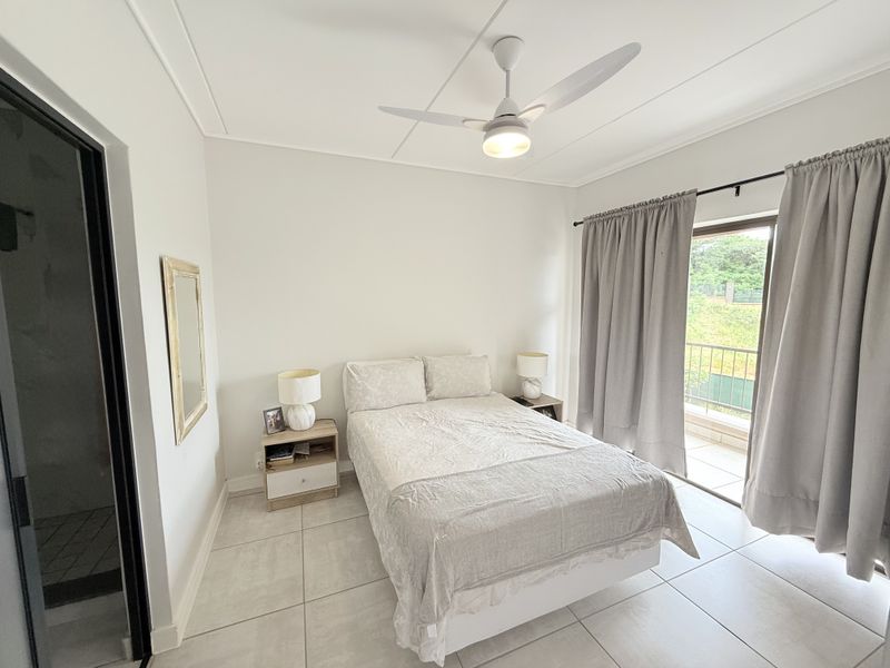 A bright bedroom featuring tiled flooring, a ceiling fan, and direct access to a private balcony through sliding glass doors.