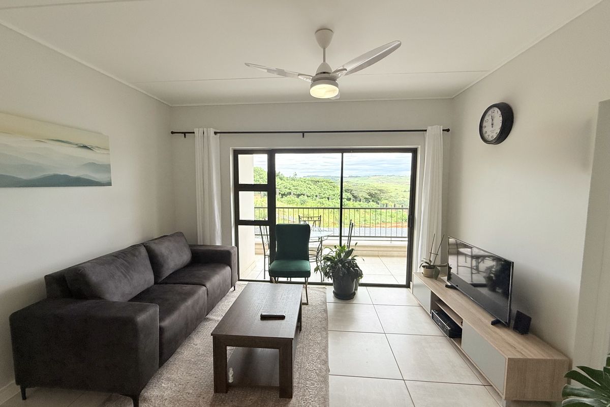 A bright living room featuring tiled flooring, a ceiling fan, and large sliding glass doors that open onto a balcony with scenic views.