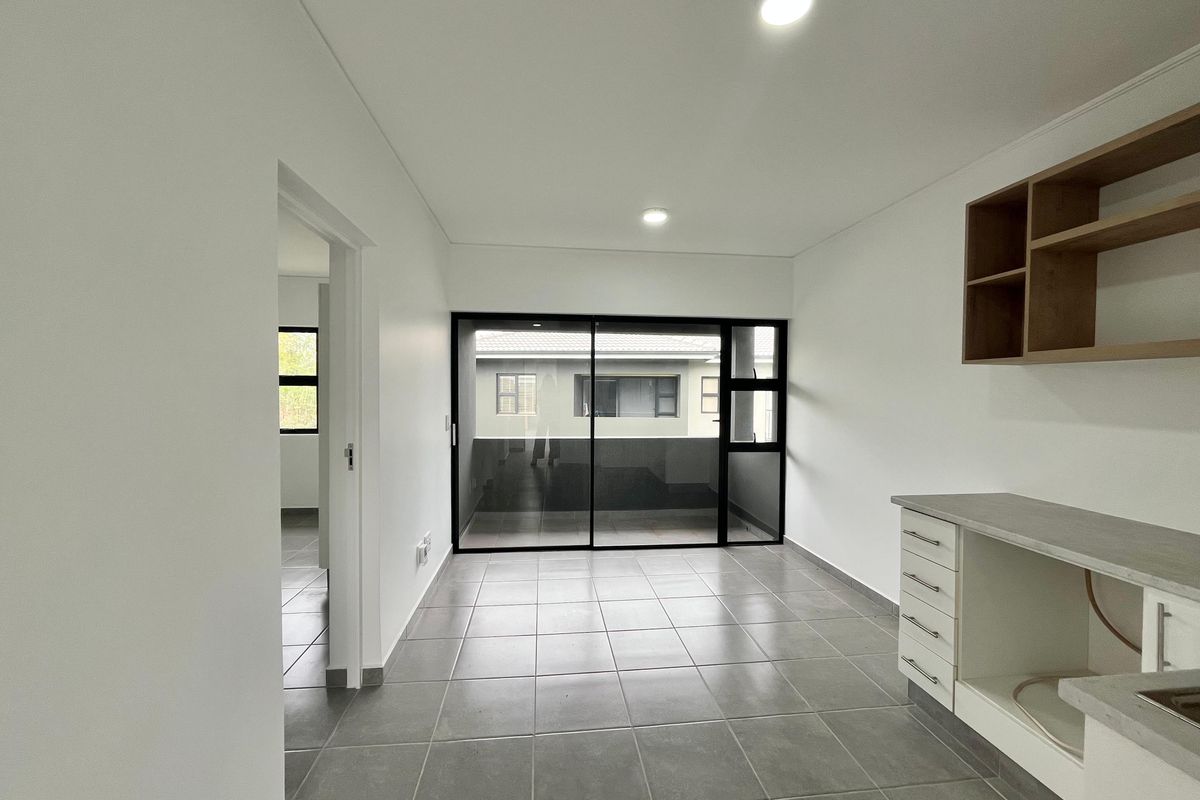 A bright, modern kitchen area featuring neutral tiled flooring, built-in cabinetry with laminate countertops, and a large sliding glass door leading to an outdoor space.