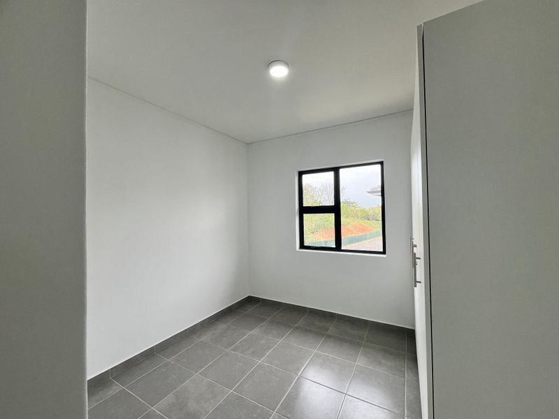 A clean, empty bedroom featuring neutral tiled flooring, a built-in cupboard, and a modern aluminium-framed window providing natural light.