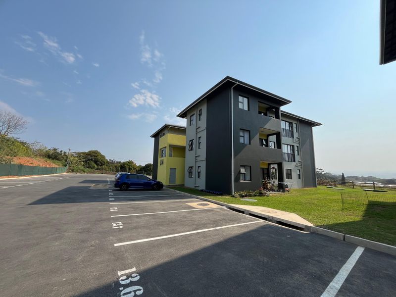 Exterior view of a modern multi-story apartment building featuring a paved parking area, landscaped grounds, and private balconies.