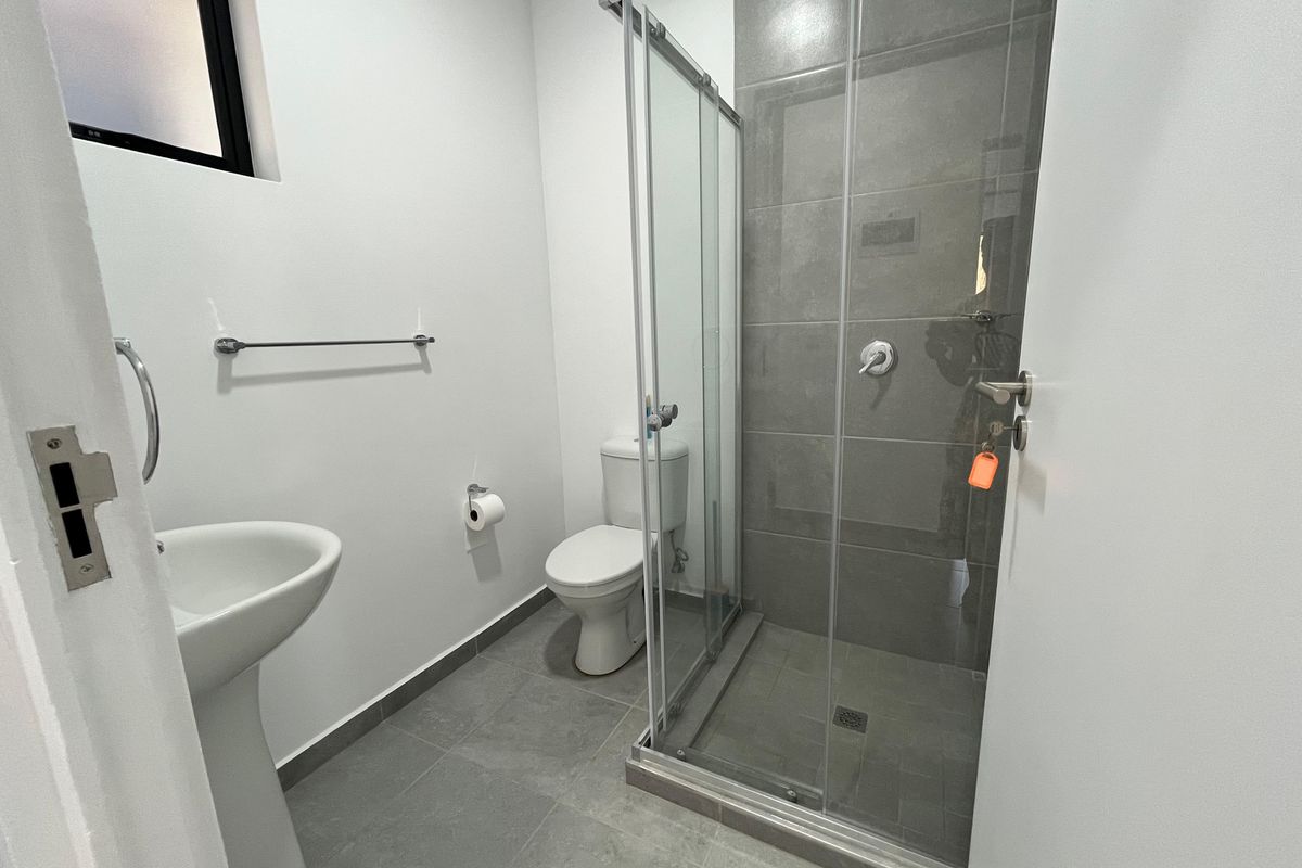 A modern, clean bathroom featuring a pedestal sink, a toilet, and a glass-enclosed shower with grey floor and wall tiling.