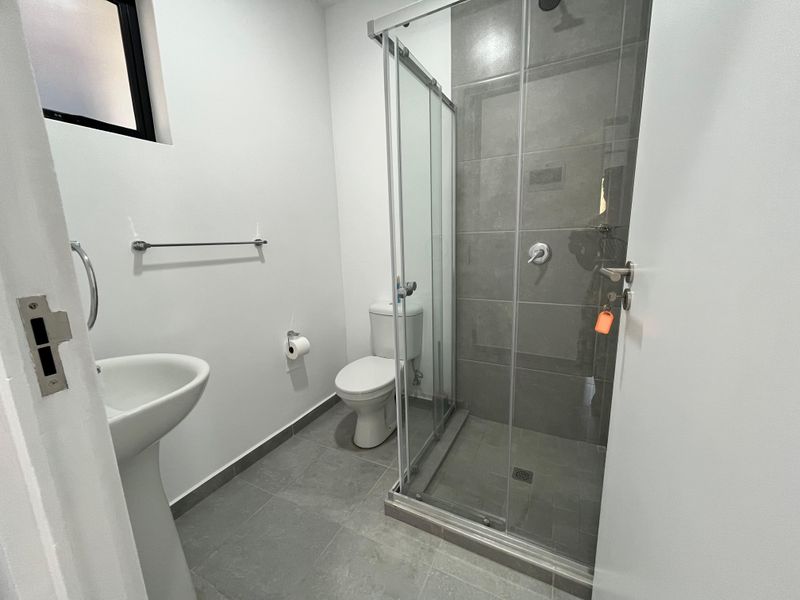 A modern, clean bathroom featuring a pedestal sink, a toilet, and a glass-enclosed shower with grey floor and wall tiling.