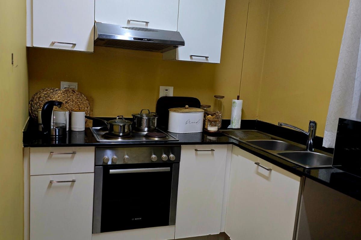 Compact kitchen featuring white cabinetry, granite countertops, stainless steel sink, and built-in oven with extractor fan.