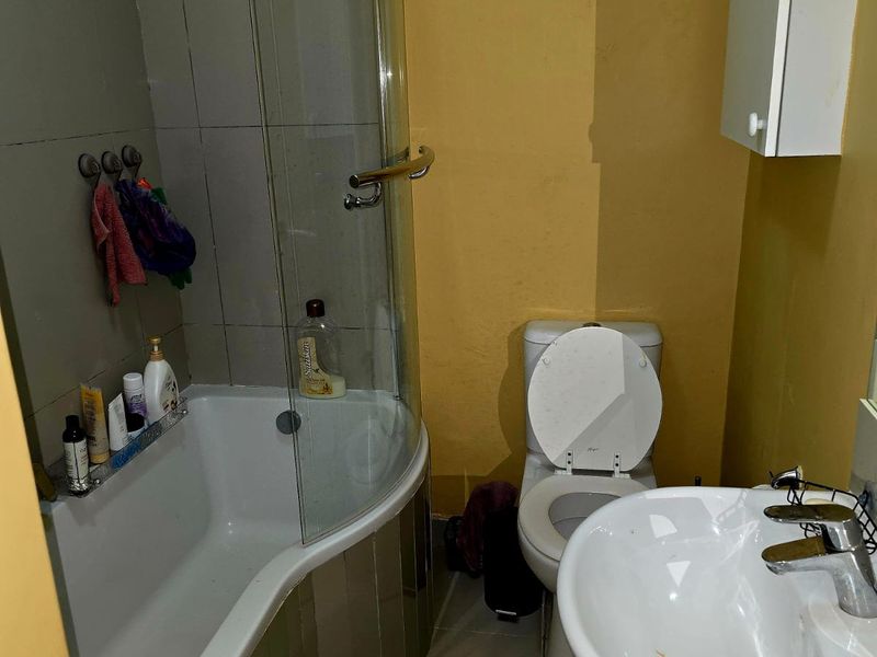 Compact bathroom featuring a curved shower-bath combination, pedestal basin, and toilet, requiring cosmetic updates to the wall finishes.