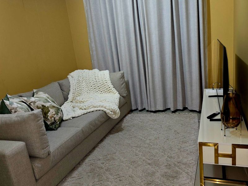 A cozy living room featuring neutral tiled flooring, coved ceiling details, and a curtained window, creating a comfortable and well-maintained living space.