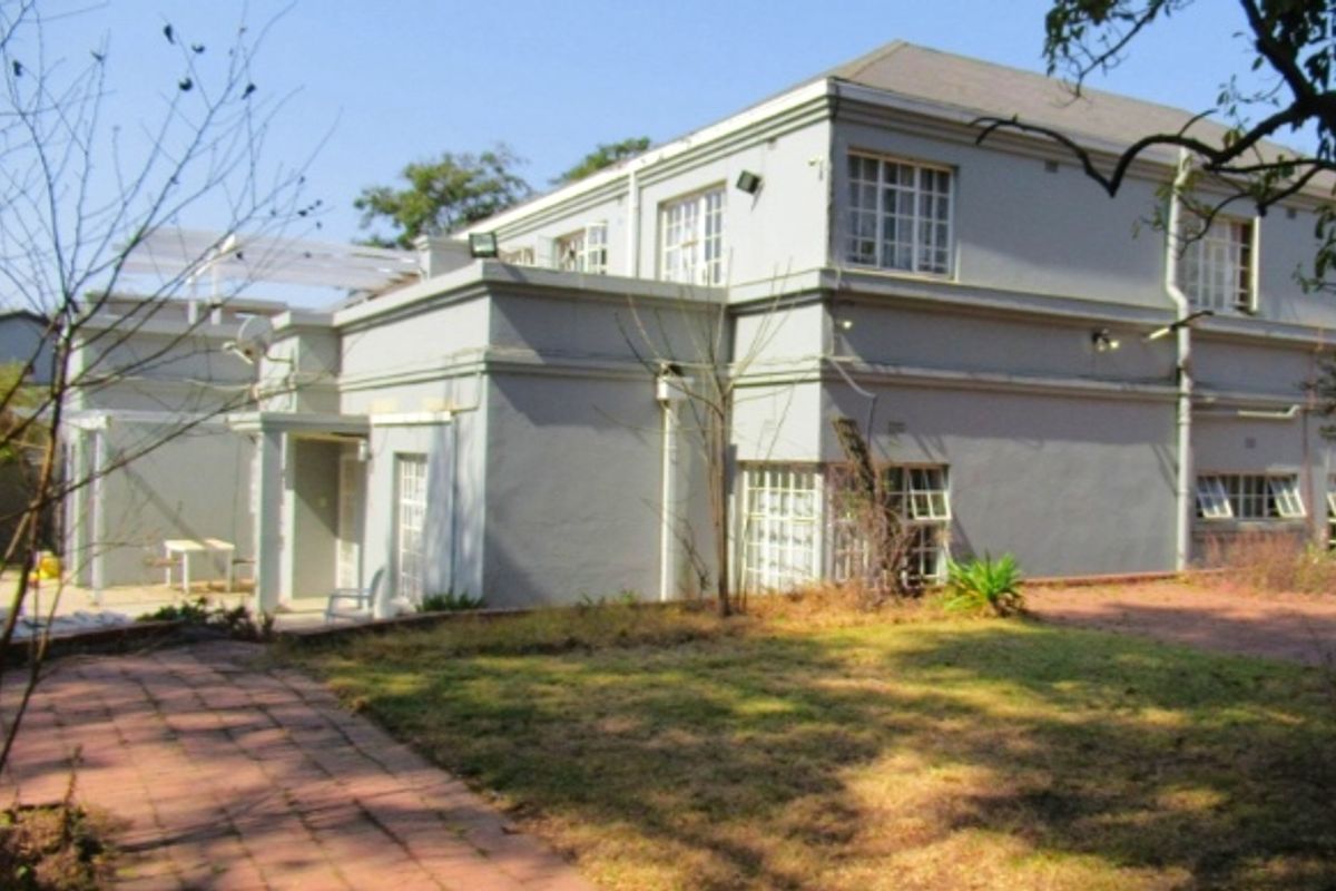 Rear view of a multi-story residential property featuring a paved walkway and garden area, showing signs of exterior wear and maintenance requirements.