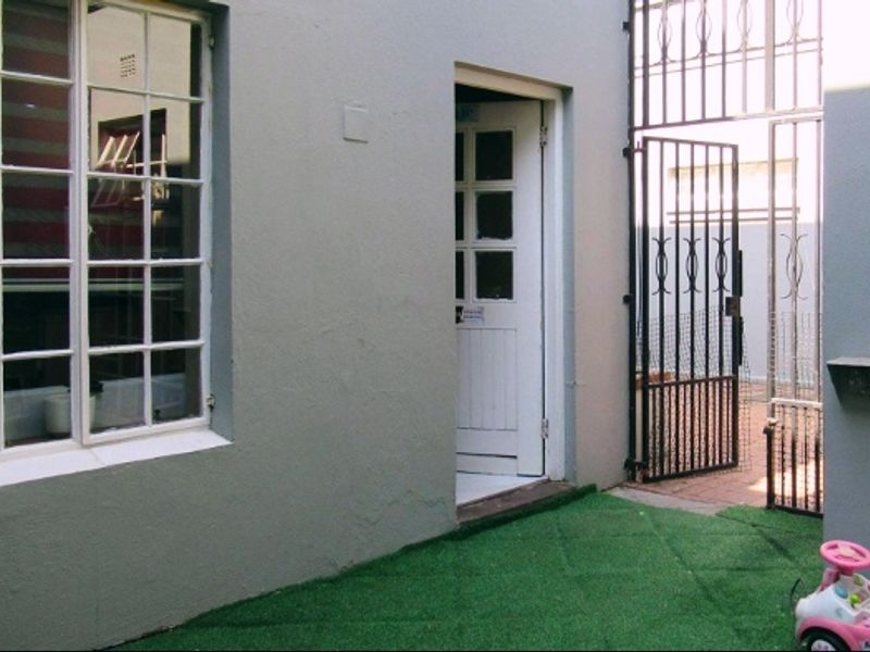 A rear exterior view showing a paved area with artificial turf, a security gate, and access to the home through a multi-pane door.
