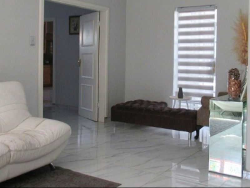 A bright living room featuring polished marble-look floor tiles, a staircase with tiled steps, and modern roller blinds.