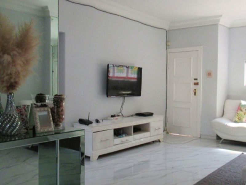 A living room featuring tiled flooring, coved ceilings, and a panelled door, with visible wall-mounted television and exposed wiring.