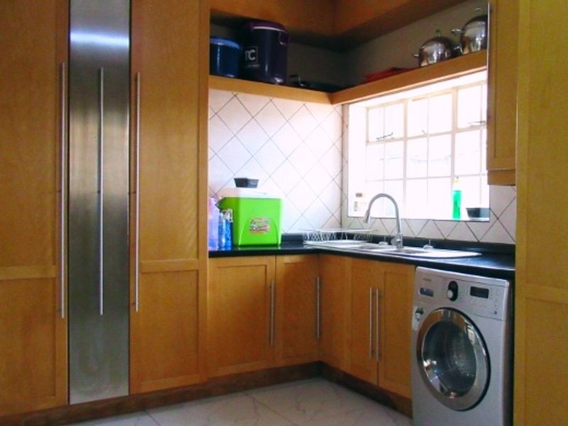A functional kitchen featuring wooden cabinetry, a stainless steel sink with mixer tap, tiled backsplash, and tiled flooring.