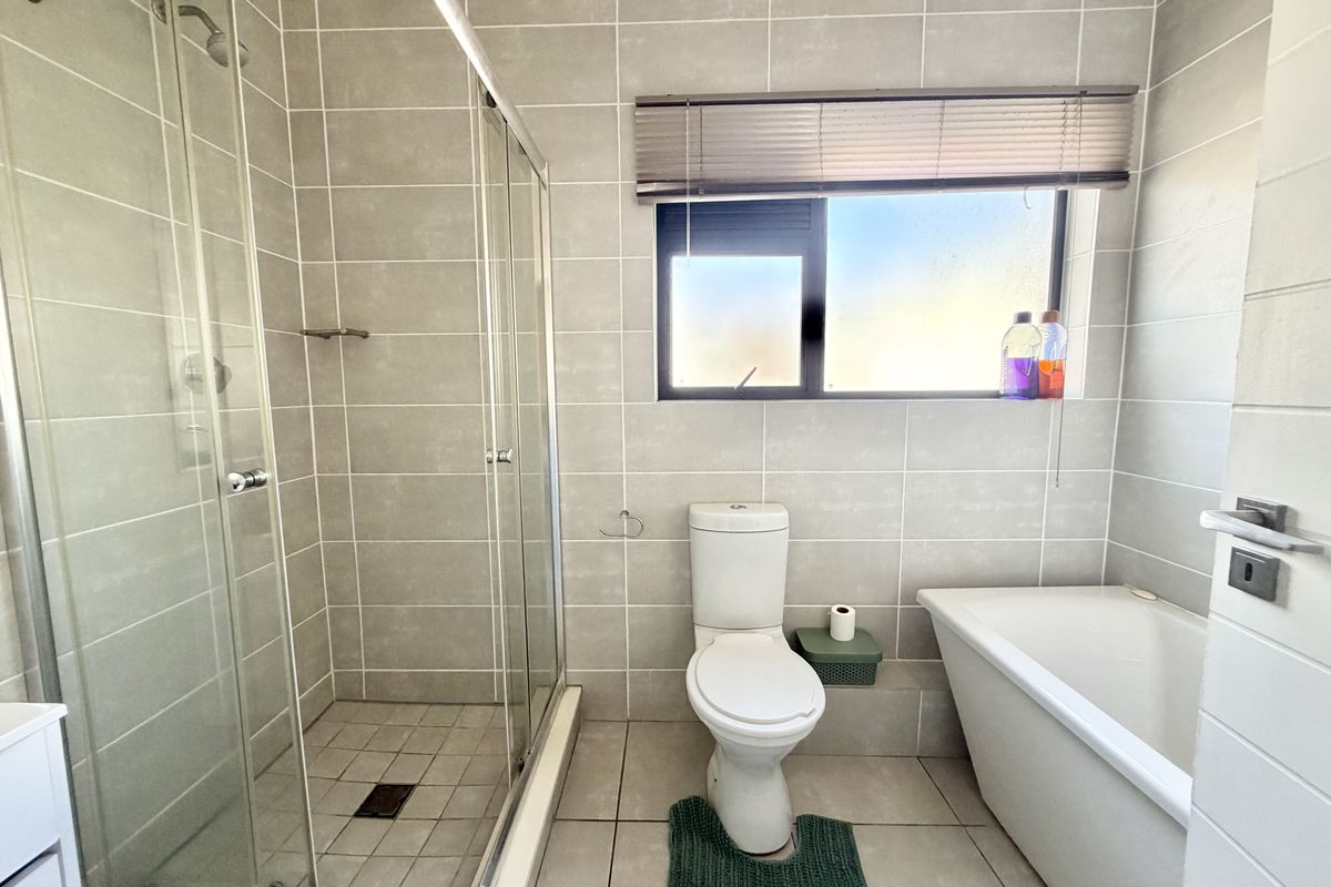 A modern bathroom featuring a glass-enclosed shower, a freestanding bathtub, and neutral wall-to-floor tiling with natural light from a window.