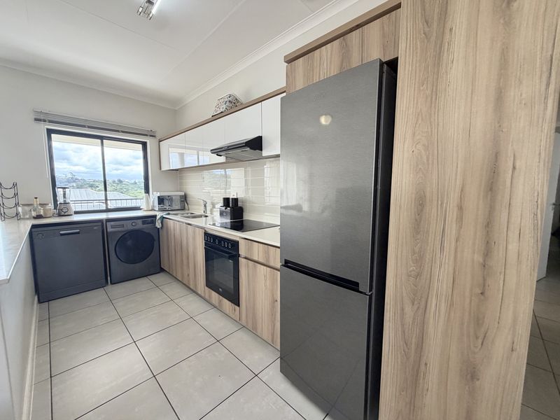 Modern kitchen featuring wood-grain cabinetry, sleek white upper cabinets, subway tile backsplash, integrated appliances, and large format floor tiles.