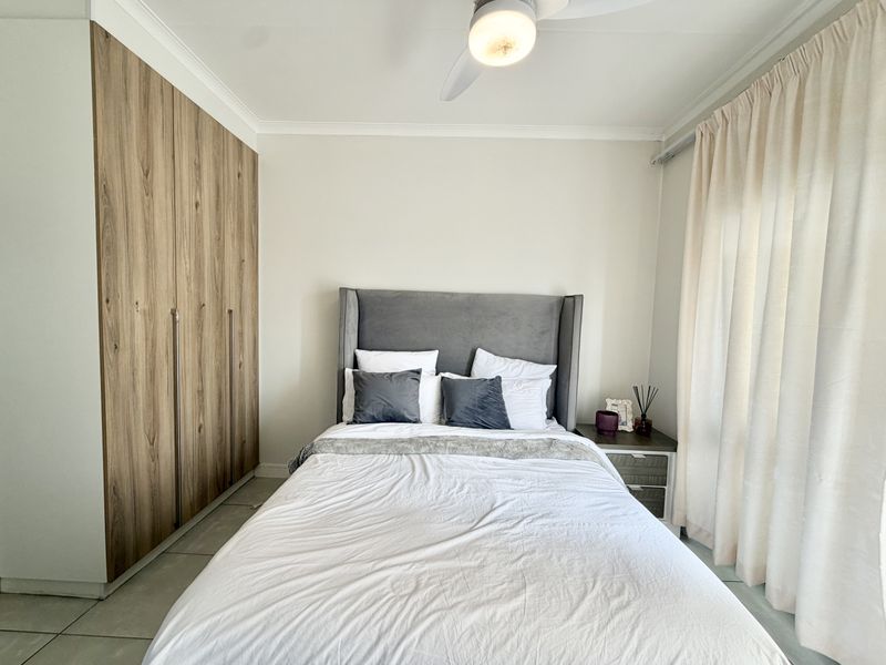 A well-maintained bedroom featuring modern wood-finish built-in cupboards, tiled flooring, and a ceiling fan, offering a clean and functional living space.