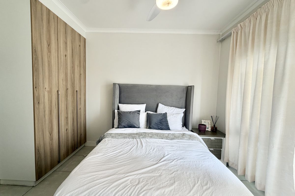 A well-maintained bedroom featuring modern wood-finish built-in cupboards, tiled flooring, and a ceiling fan, offering a clean and functional living space.