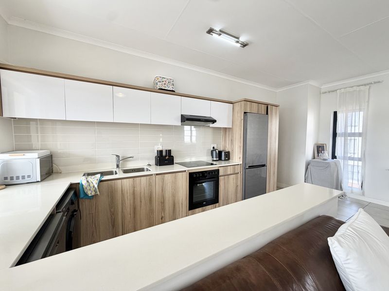 Modern kitchen featuring sleek white and wood-grain cabinetry, quartz countertops, integrated appliances, and a functional breakfast bar overlooking the living area.