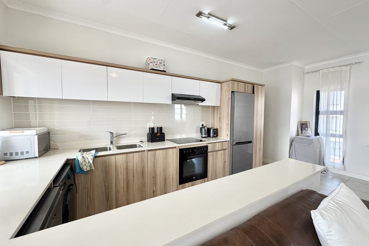 Modern kitchen featuring sleek white and wood-grain cabinetry, quartz countertops, integrated appliances, and a functional breakfast bar overlooking the living area.