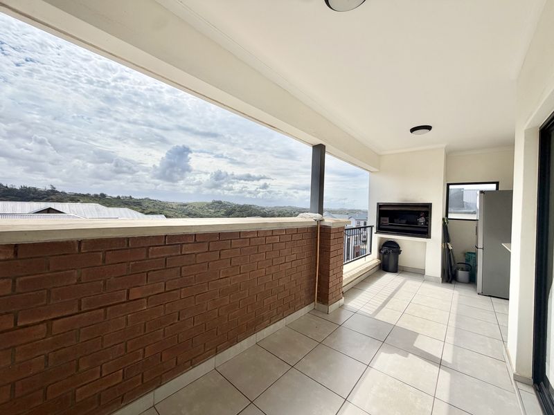 Spacious covered balcony featuring a built-in braai, tiled flooring, and a brick parapet wall with expansive elevated views.