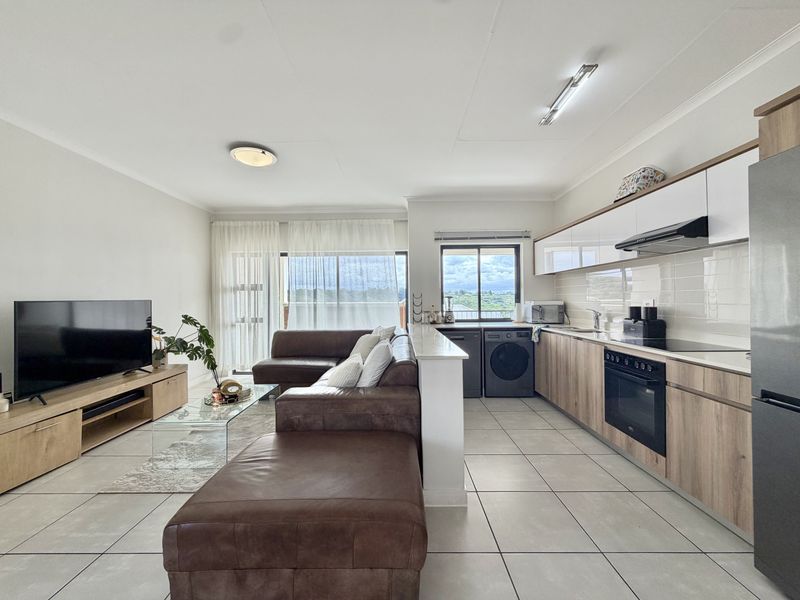 Modern open-plan living area featuring a contemporary kitchen with wood-finish cabinetry, integrated appliances, and seamless flow to a bright lounge with balcony access.