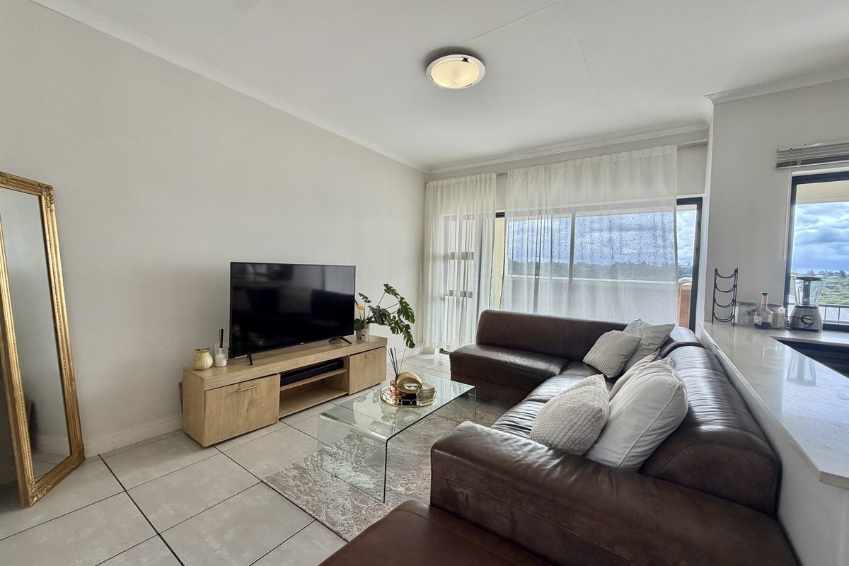 A bright living room featuring large format floor tiles, a coved ceiling, and a sliding glass door providing access to the balcony.