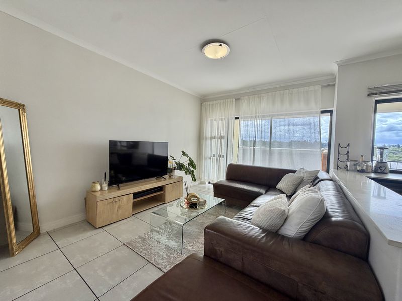 A bright living room featuring large format floor tiles, a coved ceiling, and a sliding glass door providing access to the balcony.