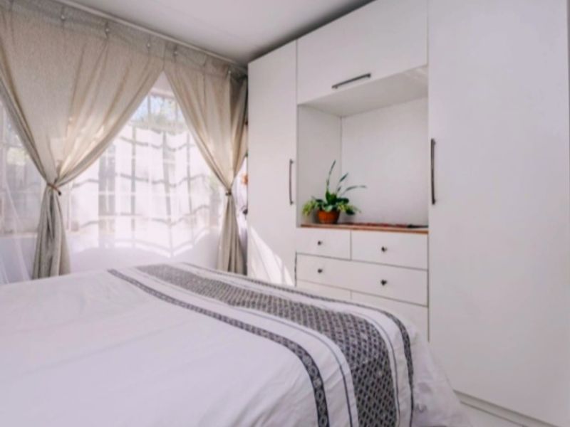 A well-maintained bedroom featuring built-in white cabinetry with integrated drawers and tiled flooring, offering a clean and functional living space.