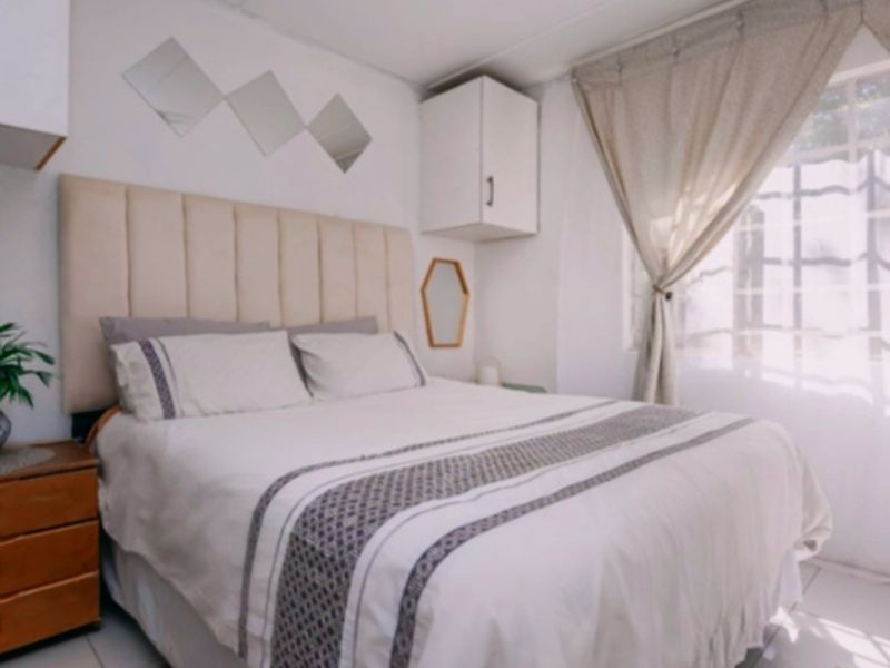 A cozy bedroom featuring tiled flooring, built-in wall cabinetry for storage, and a window fitted with security bars.