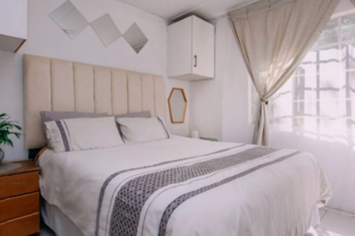 A cozy bedroom featuring tiled flooring, built-in wall cabinetry for storage, and a window fitted with security bars.