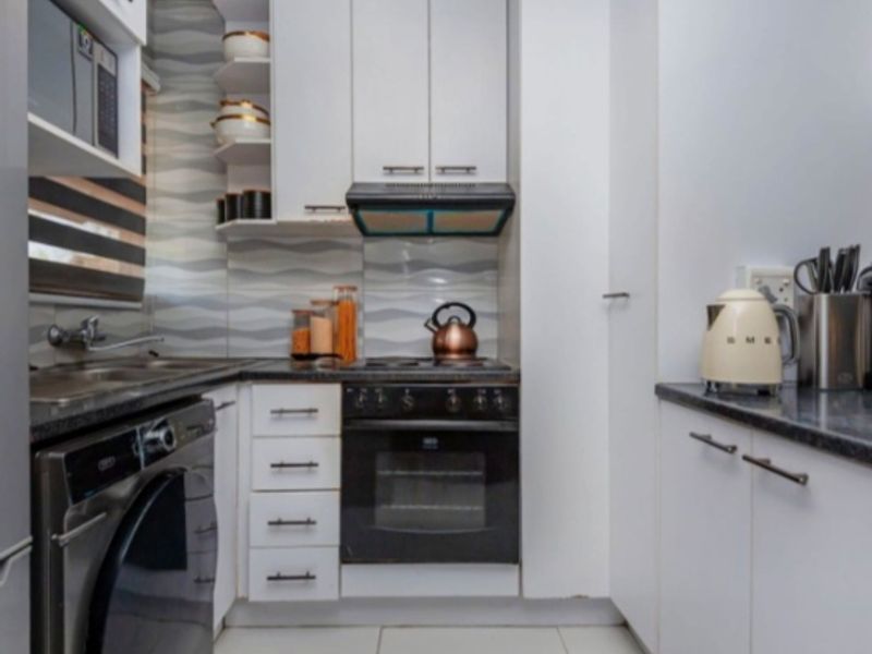Compact modern kitchen featuring white cabinetry, dark countertops, built-in oven, electric hob, extractor fan, and tiled backsplash.