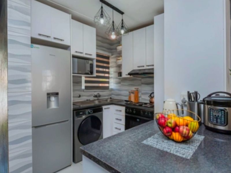 Modern compact kitchen featuring white cabinetry, dark stone countertops, integrated appliances, tiled backsplash, and stylish pendant lighting.
