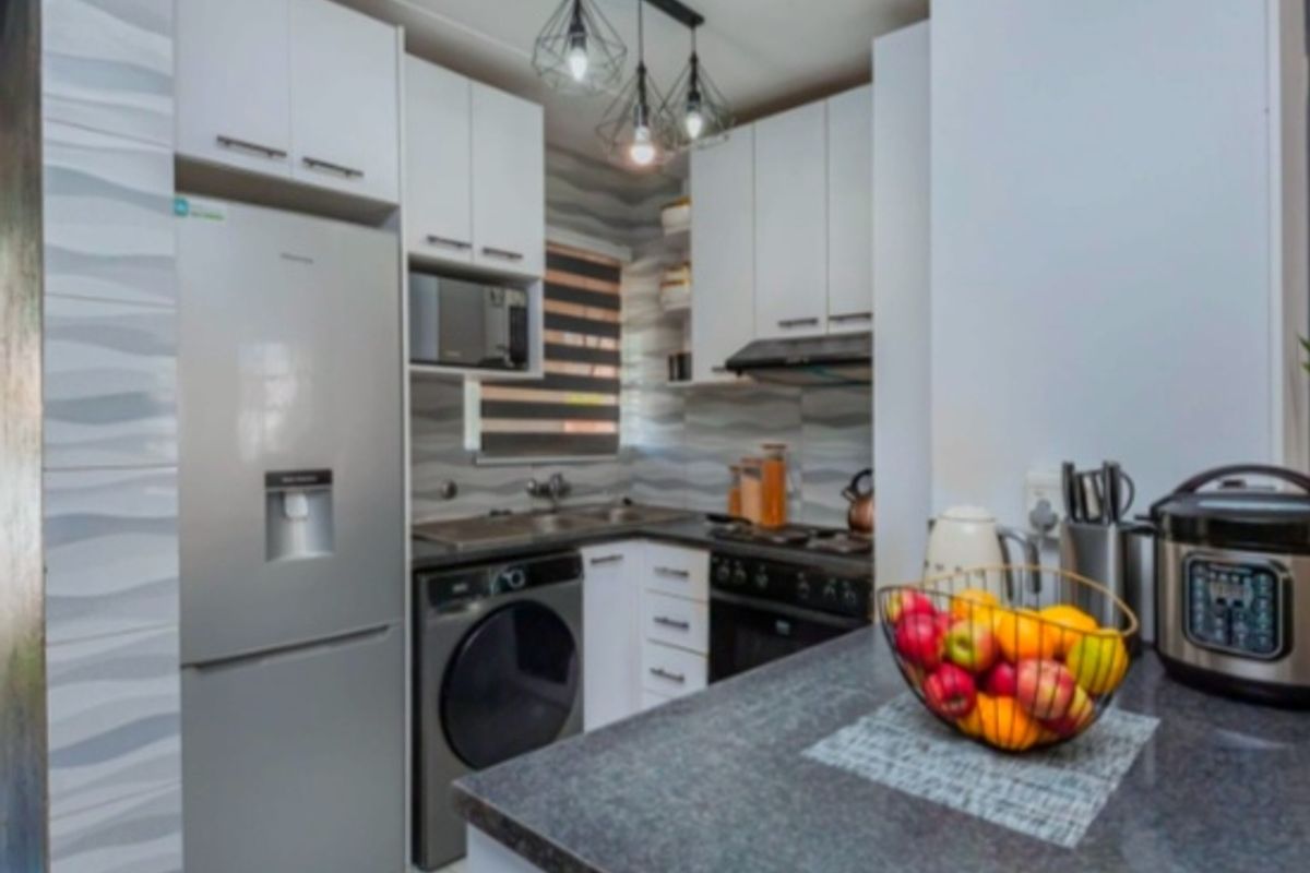 Modern compact kitchen featuring white cabinetry, dark stone countertops, integrated appliances, tiled backsplash, and stylish pendant lighting.