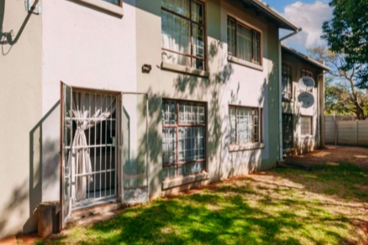 Rear view of a multi-story apartment building featuring security gates, aluminium window frames, and a small private garden area.