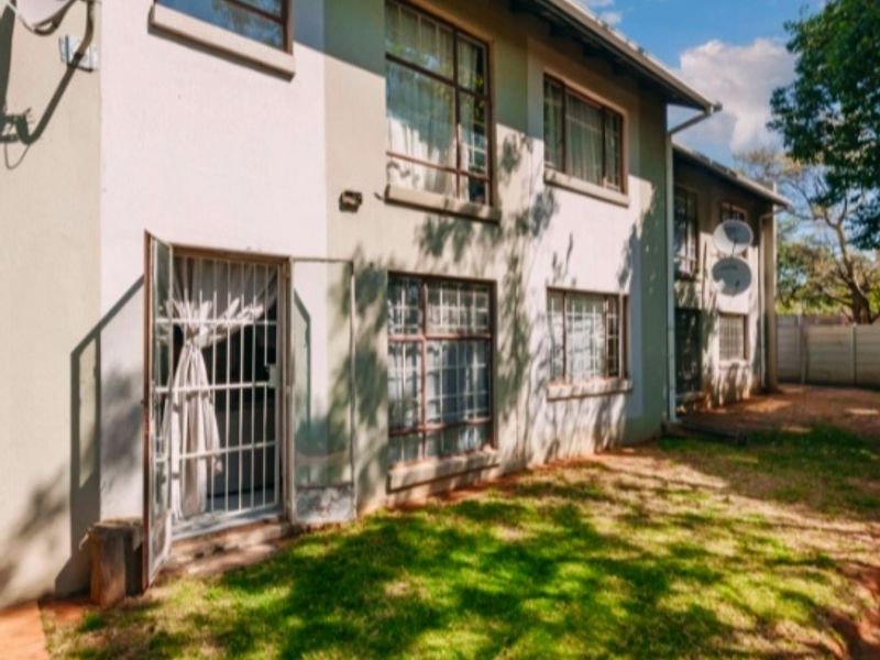 Rear view of a multi-story apartment building featuring security gates, aluminium window frames, and a small private garden area.